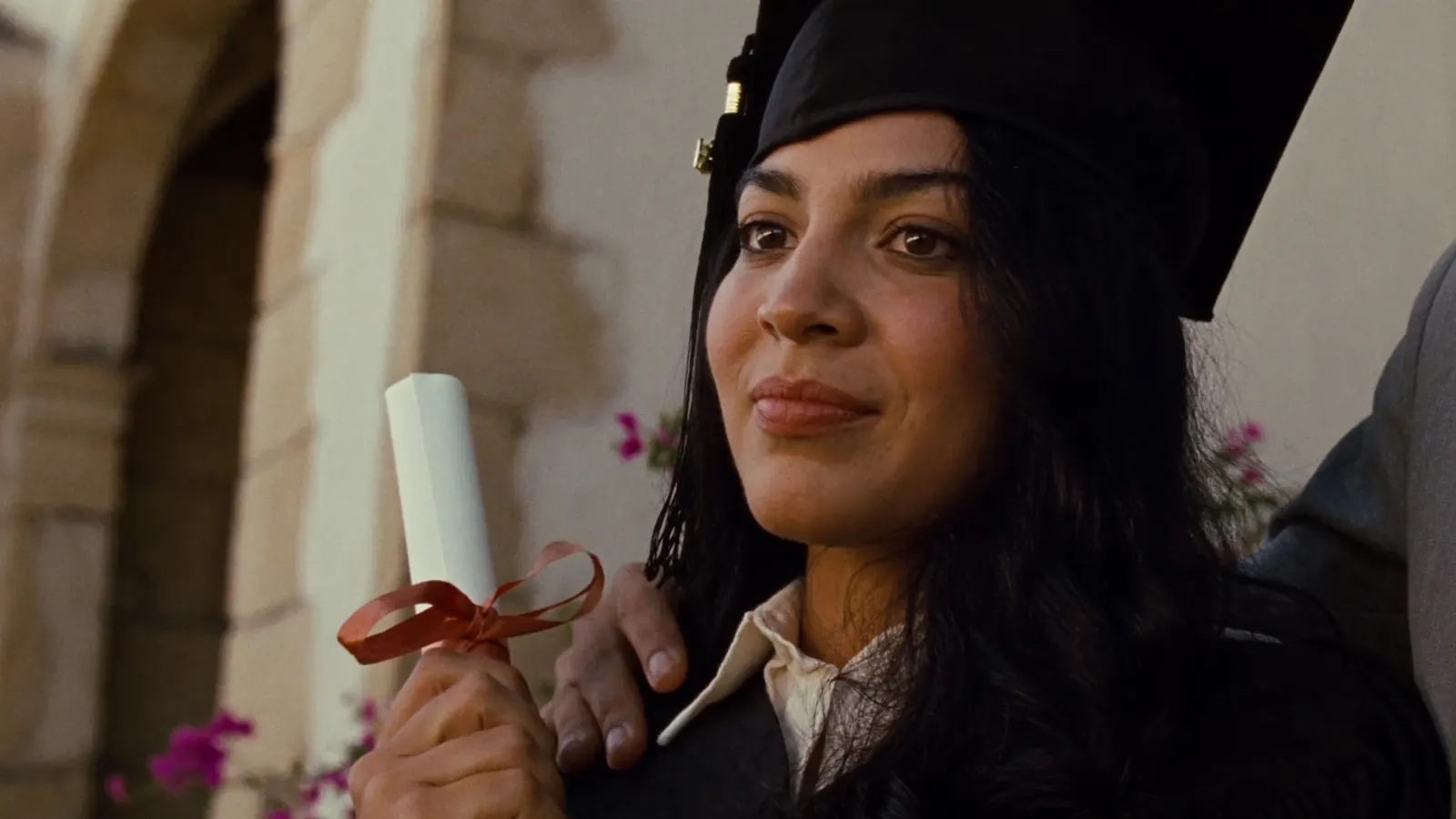 A graduate holding her diploma with her mother's hand on her shoulder
